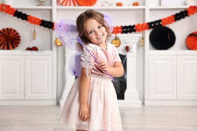 Photo of Cute girl dressed like fairy with magic wand in room. Halloween costume