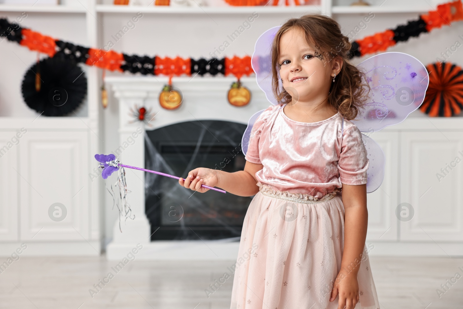 Photo of Cute girl dressed like fairy with magic wand in room. Halloween costume