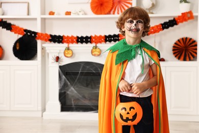 Photo of Funny boy with bucket dressed like pumpkin in room, space for text. Halloween celebration