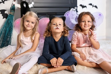 Photo of Cute girls wearing costumes for Halloween celebration in room