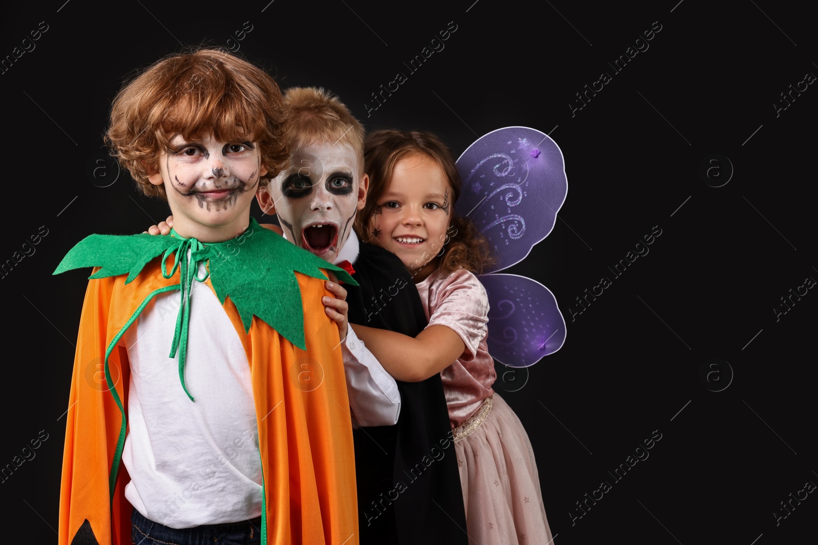 Photo of Funny children wearing costumes on black background, space for text. Halloween celebration