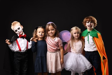 Photo of Funny children wearing costumes for Halloween celebration on black background