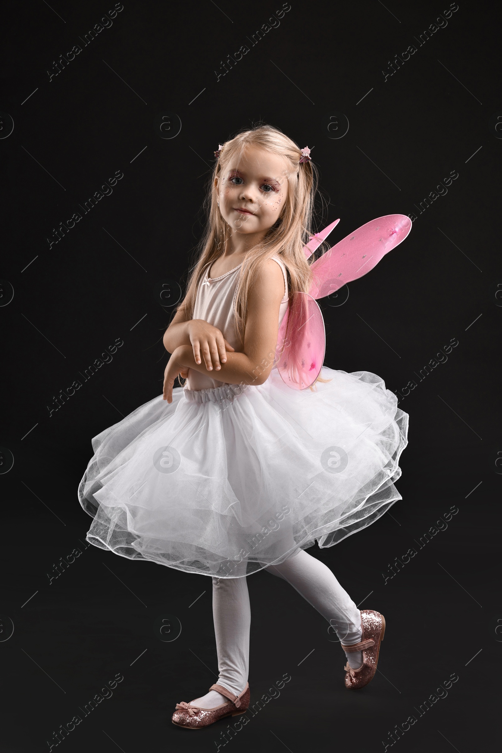 Photo of Cute girl dressed like fairy on black background. Halloween costume