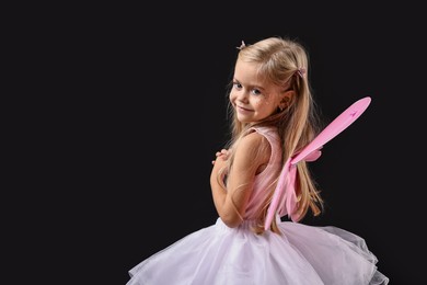 Photo of Cute girl dressed like fairy on black background, space for text. Halloween costume