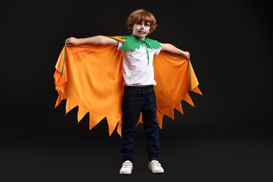 Photo of Cute boy dressed like pumpkin for Halloween celebration on black background