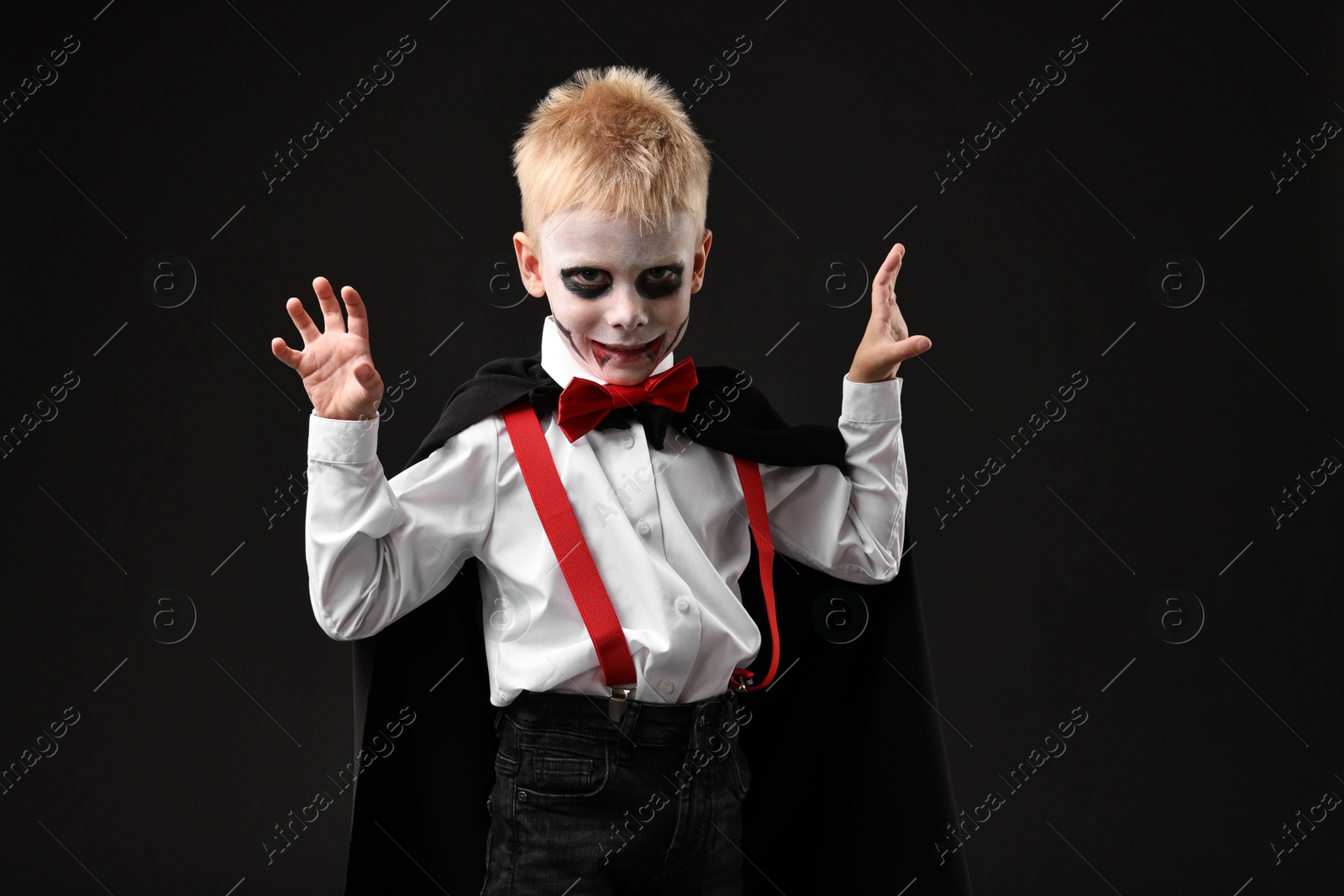 Photo of Funny boy dressed like vampire for Halloween celebration on black background