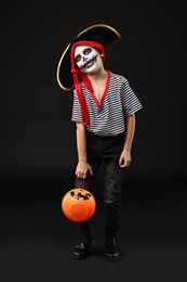 Photo of Funny boy with pumpkin bucket dressed like pirate on black background. Halloween costume