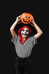 Photo of Funny boy with pumpkin bucket dressed like pirate on black background. Halloween costume