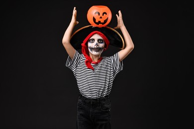 Photo of Funny boy with pumpkin bucket dressed like pirate on black background. Halloween costume