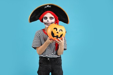 Funny boy with pumpkin bucket dressed like pirate on light blue background. Halloween costume