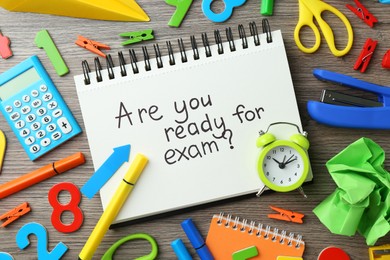 Notepad with question Are You Ready For Exam and stationery on wooden desk, flat lay