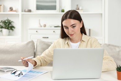 Photo of Budget planning. Young woman with papers using laptop at white table indoors