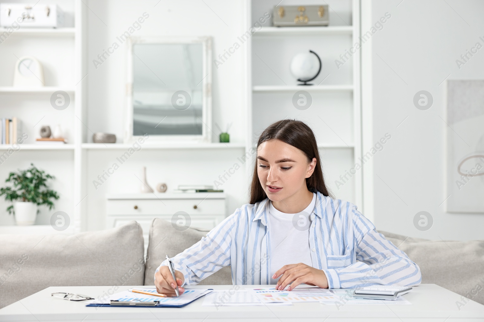 Photo of Budget planning. Beautiful young woman with papers and calculator at white table indoors