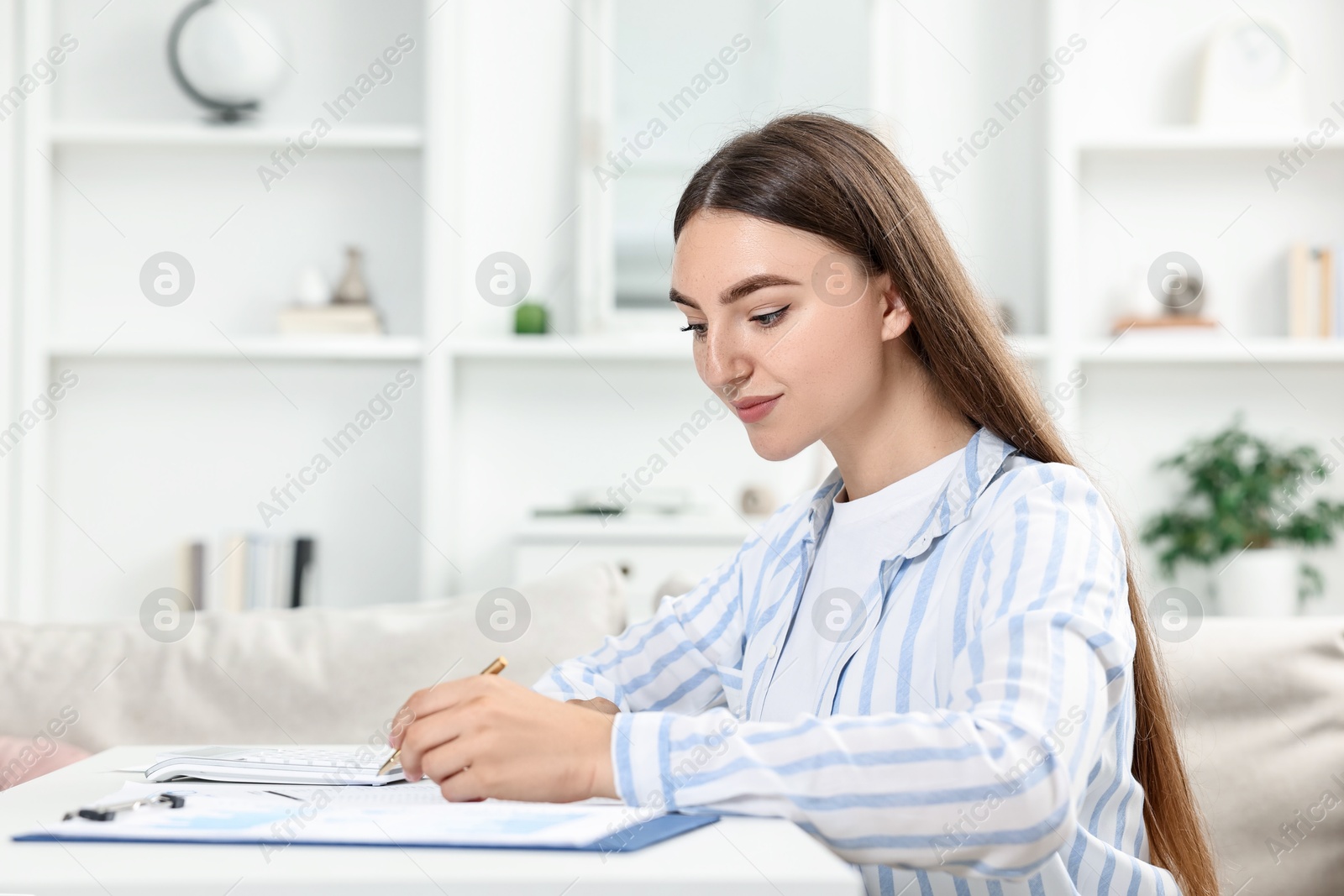 Photo of Budget planning. Beautiful young woman with papers and calculator at white table indoors