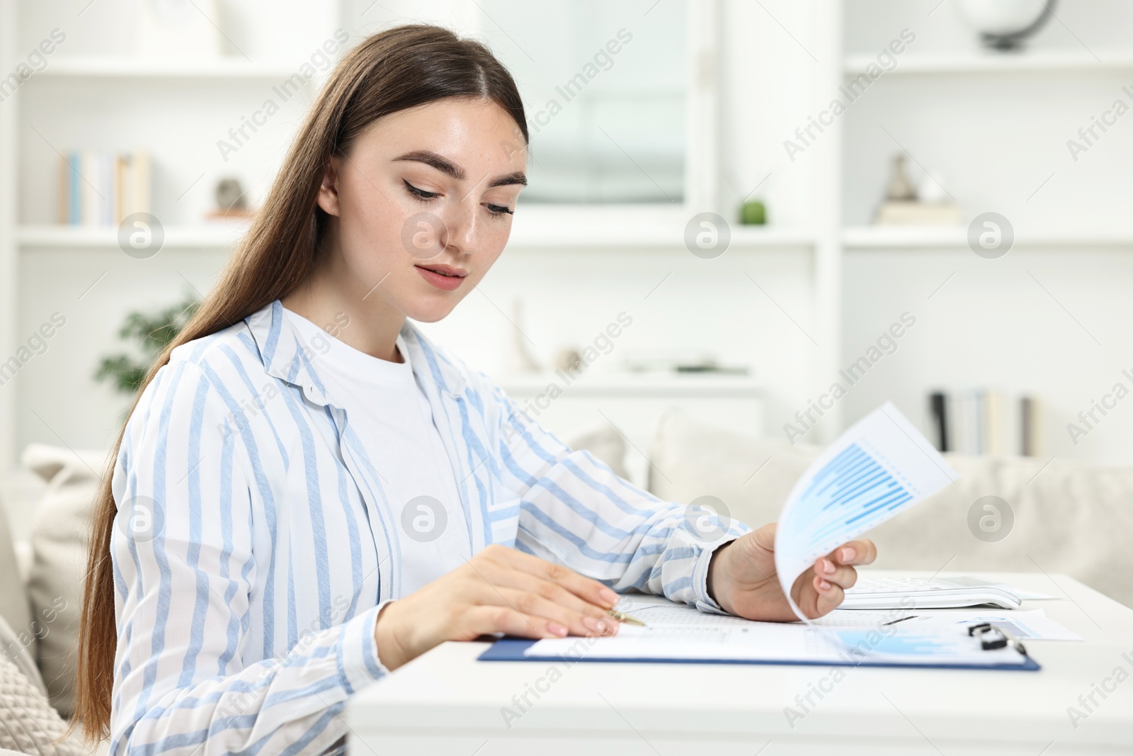 Photo of Budget planning. Beautiful young woman with papers at white table indoors