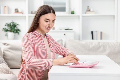 Budget planning. Beautiful young woman with papers using calculator at white table indoors