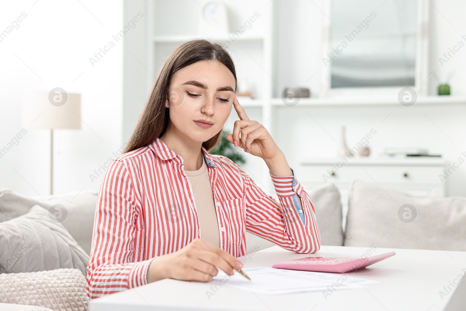 Photo of Budget planning. Beautiful young woman with papers and calculator at white table indoors