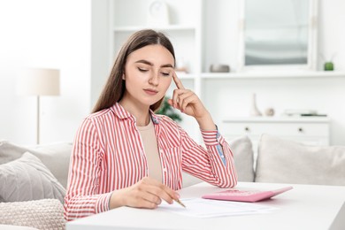 Photo of Budget planning. Beautiful young woman with papers and calculator at white table indoors