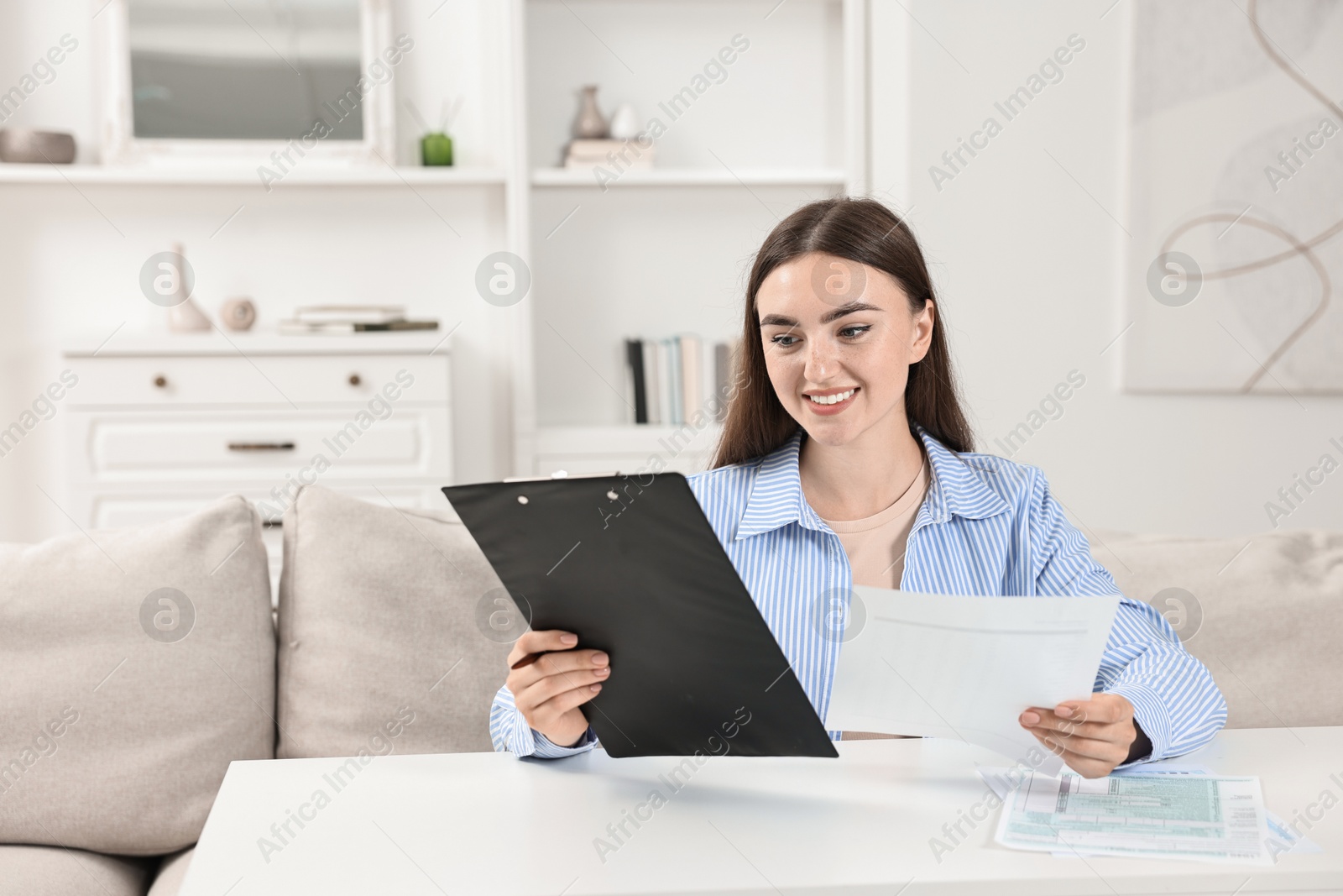 Photo of Budget planning. Beautiful young woman with papers at white table indoors