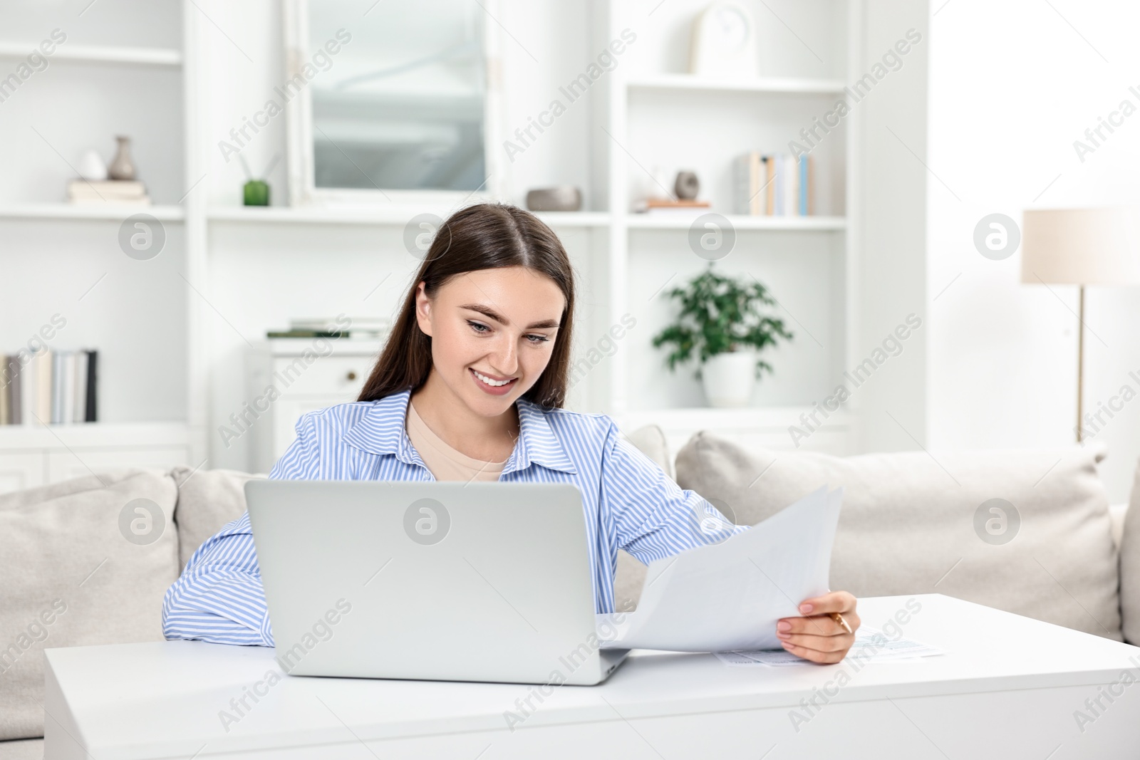 Photo of Budget planning. Young woman with papers and laptop at white table indoors