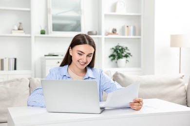 Budget planning. Young woman with papers and laptop at white table indoors