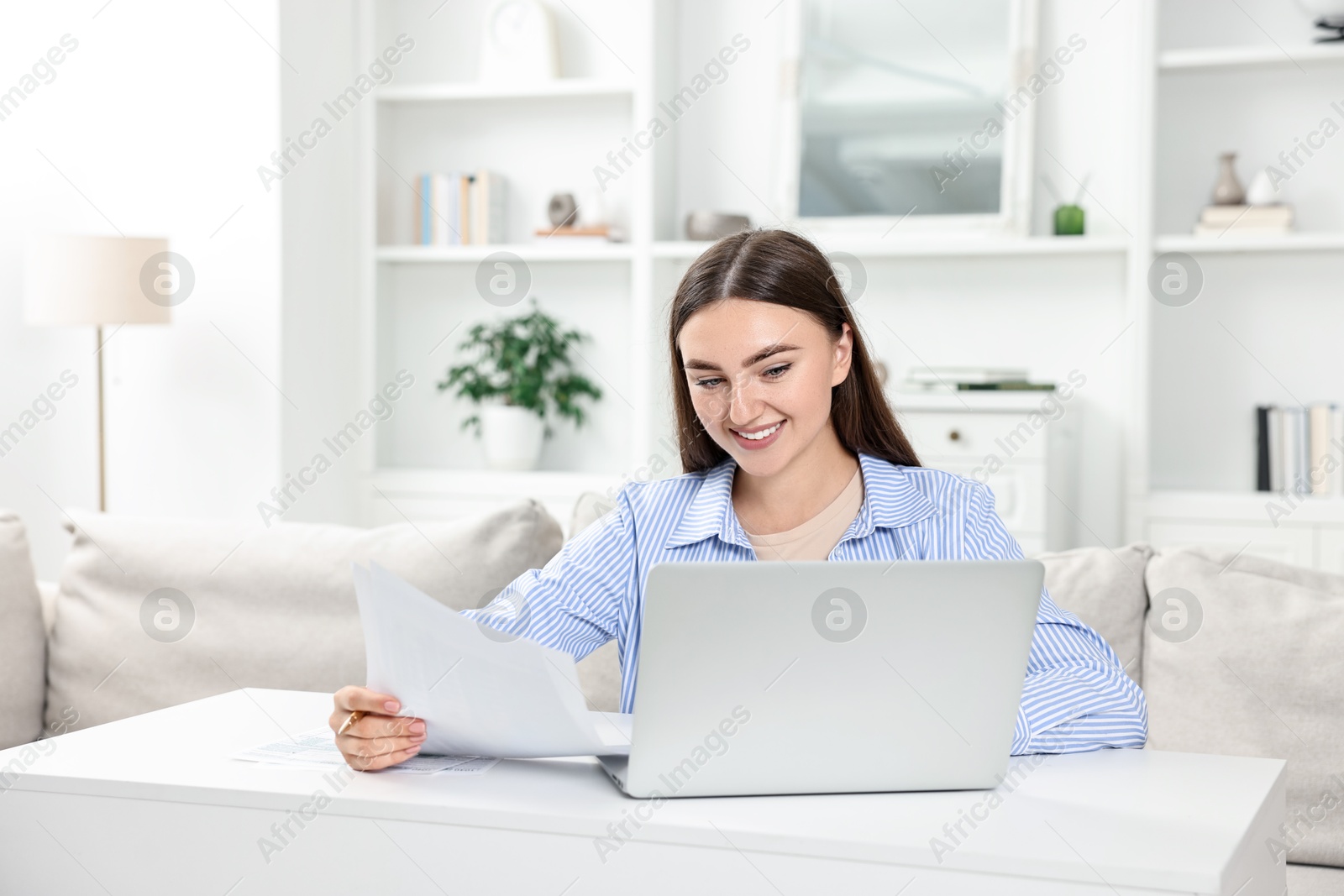 Photo of Budget planning. Young woman with papers and laptop at white table indoors