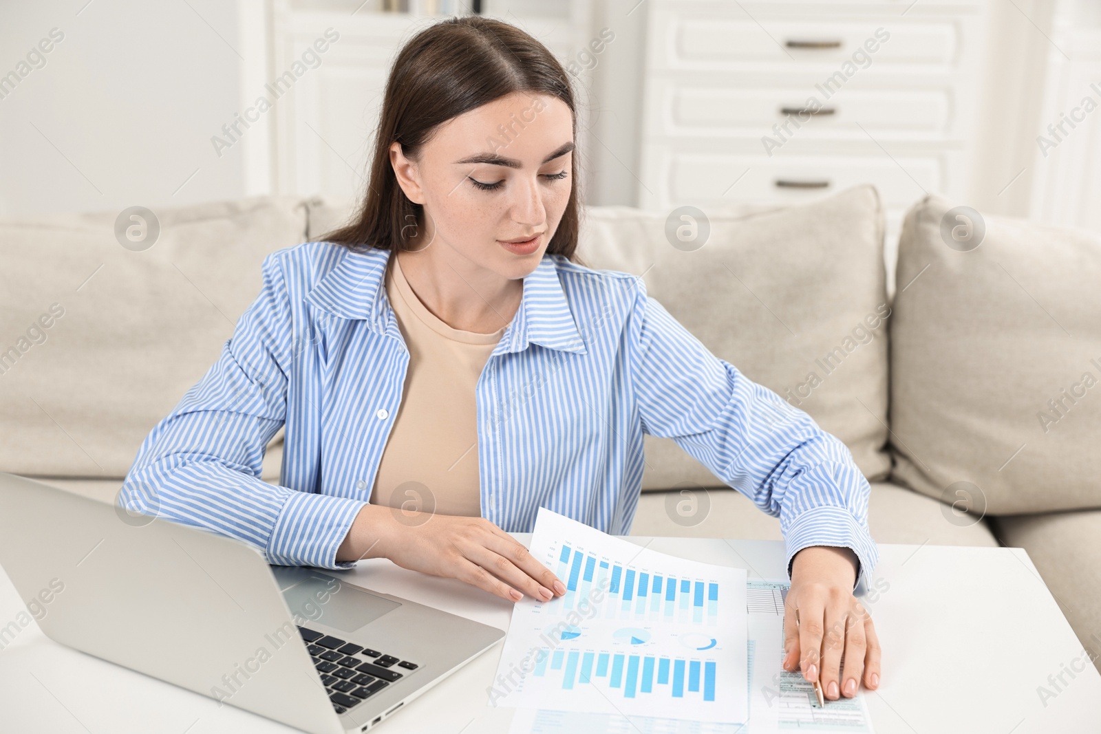 Photo of Budget planning. Beautiful young woman with papers and laptop at white table indoors