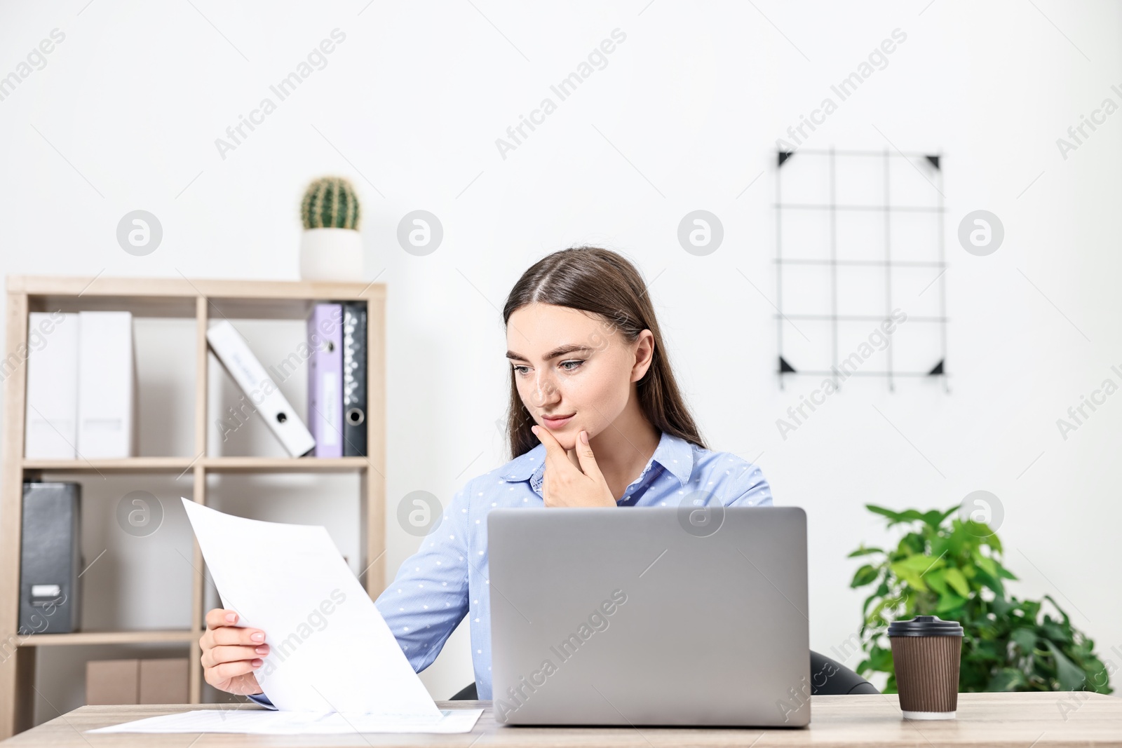 Photo of Budget planning. Beautiful young woman with papers and laptop at wooden table in office