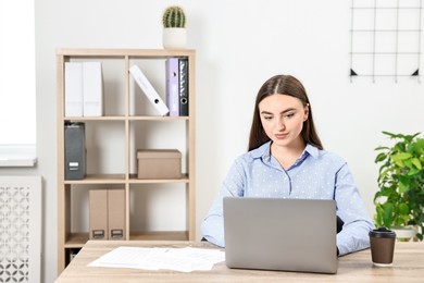 Photo of Budget planning. Beautiful young woman with papers and laptop at wooden table in office