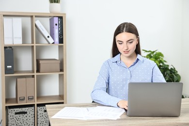 Photo of Budget planning. Beautiful young woman with papers and laptop at wooden table in office