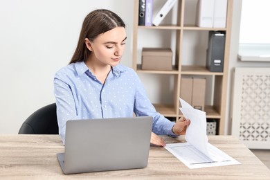 Budget planning. Beautiful young woman with papers and laptop at wooden table in office