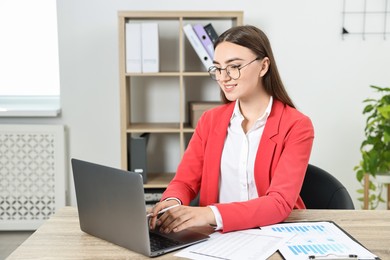 Budget planning. Young woman with papers using laptop at wooden table in office