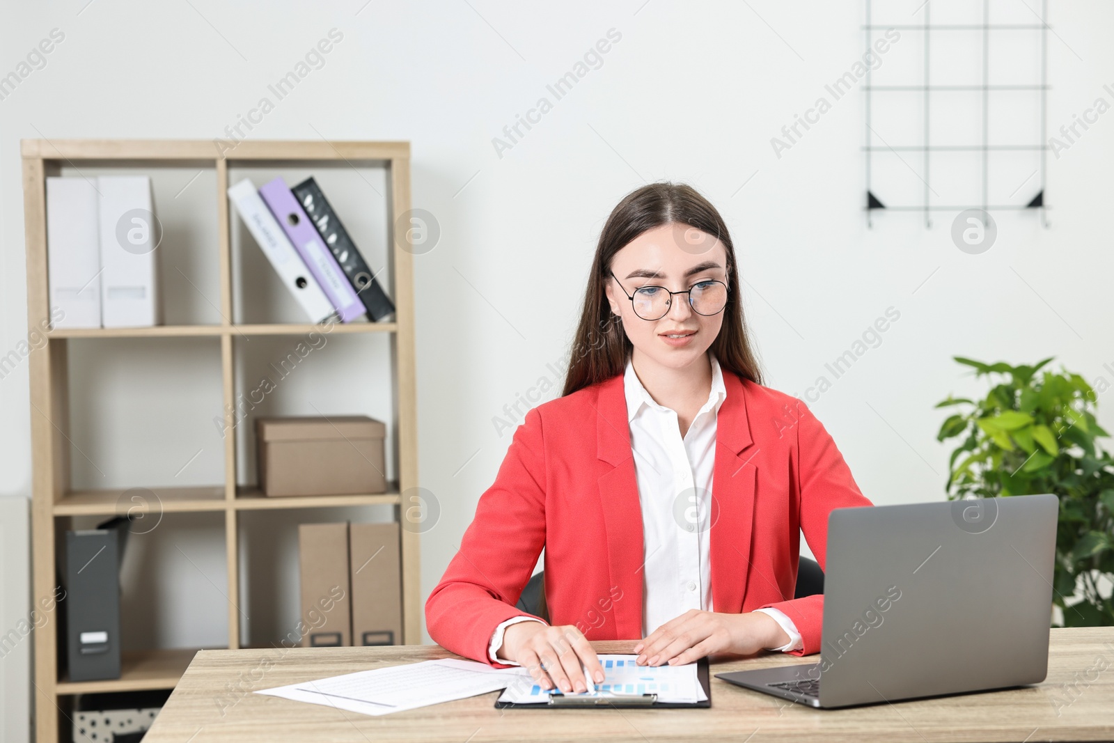 Photo of Budget planning. Young woman with papers and laptop at wooden table in office