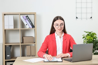 Budget planning. Young woman with papers and laptop at wooden table in office