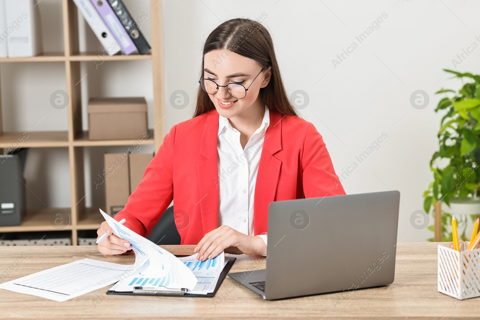 Photo of Budget planning. Young woman with papers and laptop at wooden table in office