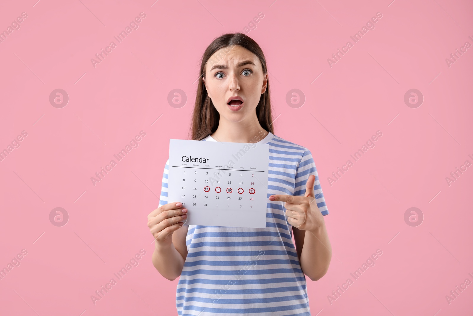 Photo of Emotional woman holding calendar with marked menstrual cycle days on pink background