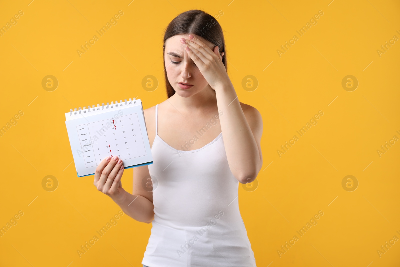 Photo of Woman holding calendar with marked menstrual cycle days on orange background