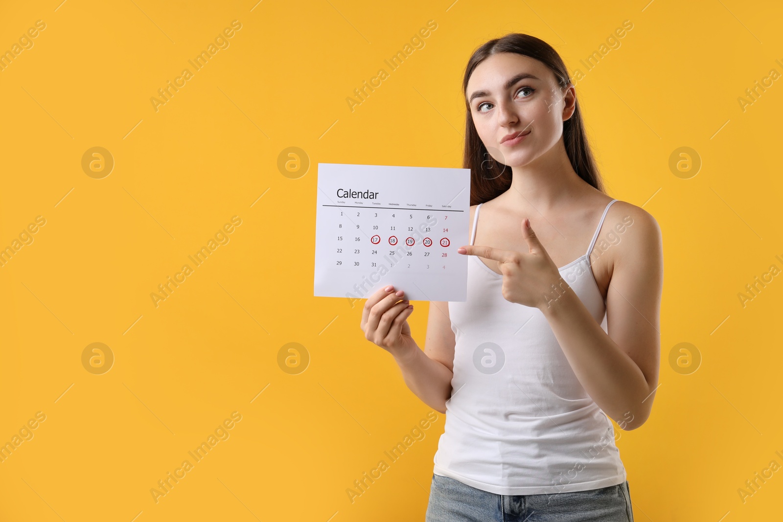 Photo of Woman holding calendar with marked menstrual cycle days on orange background, space for text