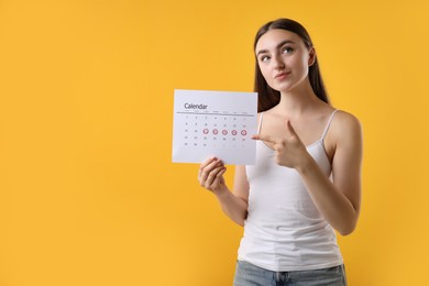 Woman holding calendar with marked menstrual cycle days on orange background, space for text