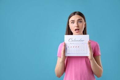 Woman holding calendar with marked menstrual cycle days on light blue background, space for text