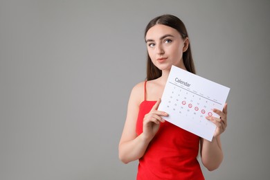 Woman holding calendar with marked menstrual cycle days on grey background, space for text