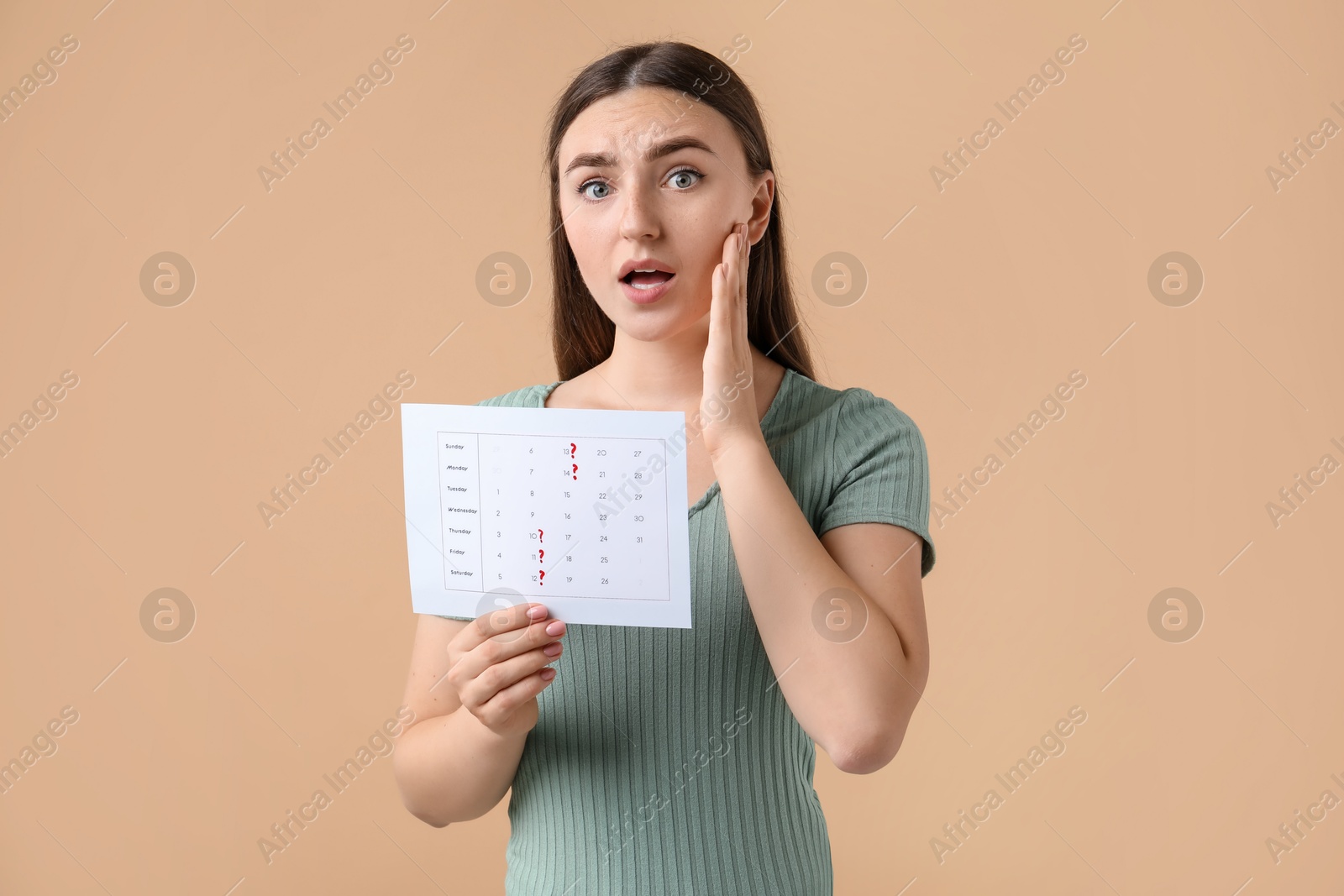 Photo of Woman holding calendar with marked menstrual cycle days on beige background