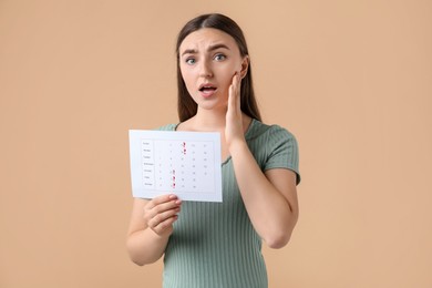 Photo of Woman holding calendar with marked menstrual cycle days on beige background