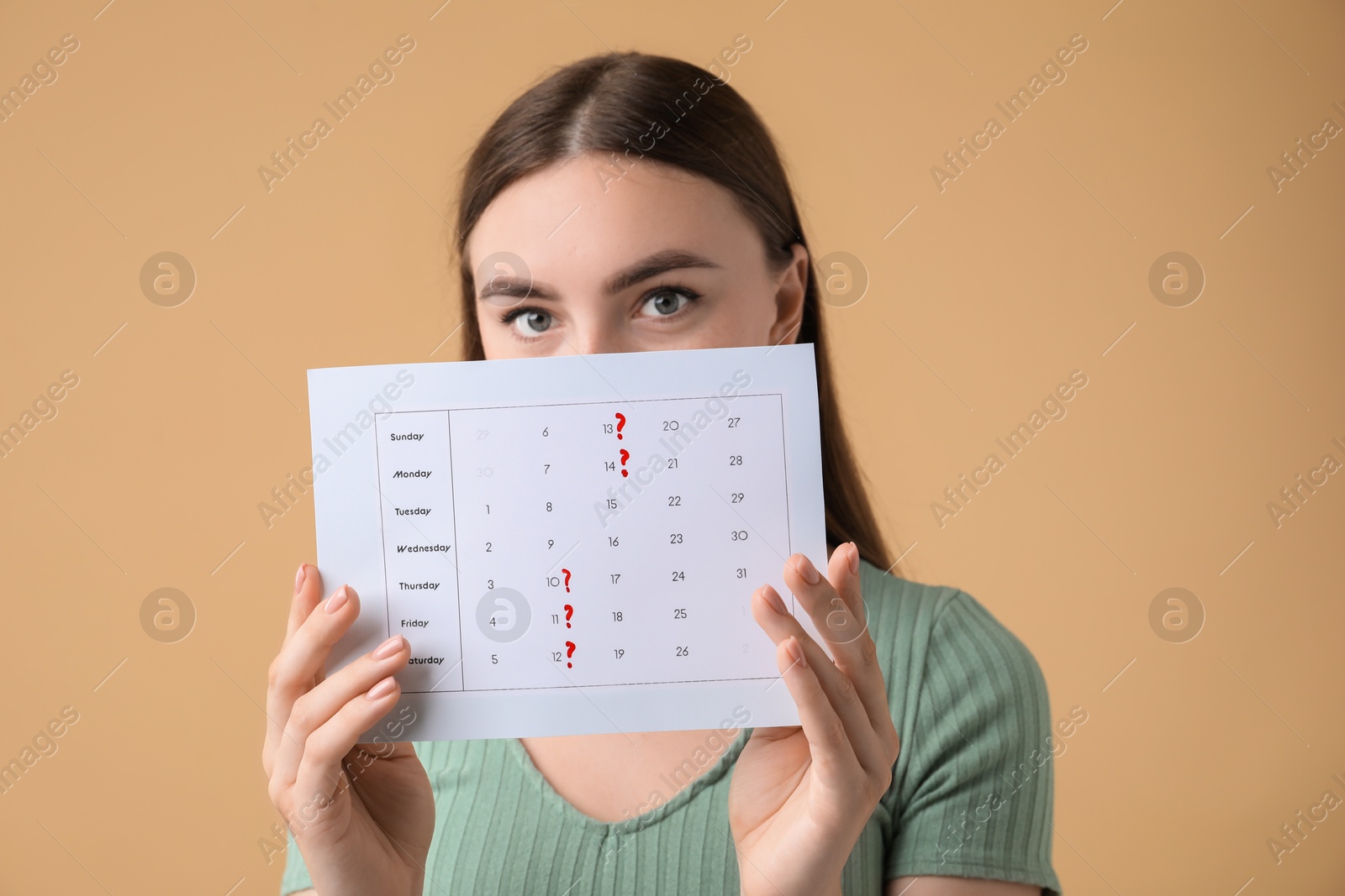 Photo of Woman holding calendar with marked menstrual cycle days on beige background