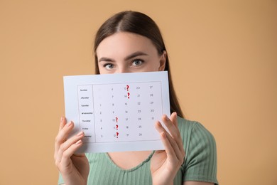 Woman holding calendar with marked menstrual cycle days on beige background