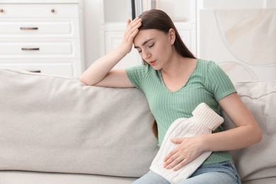 Photo of Woman using hot water bottle to relieve menstrual pain on sofa at home