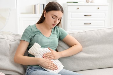 Photo of Woman using hot water bottle to relieve menstrual pain on sofa at home