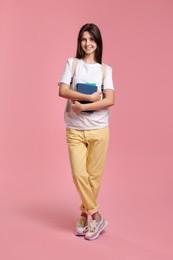 Photo of Cute teenage girl with backpack and books on pink background