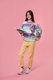 Photo of Cute teenage girl with backpack and book on pink background