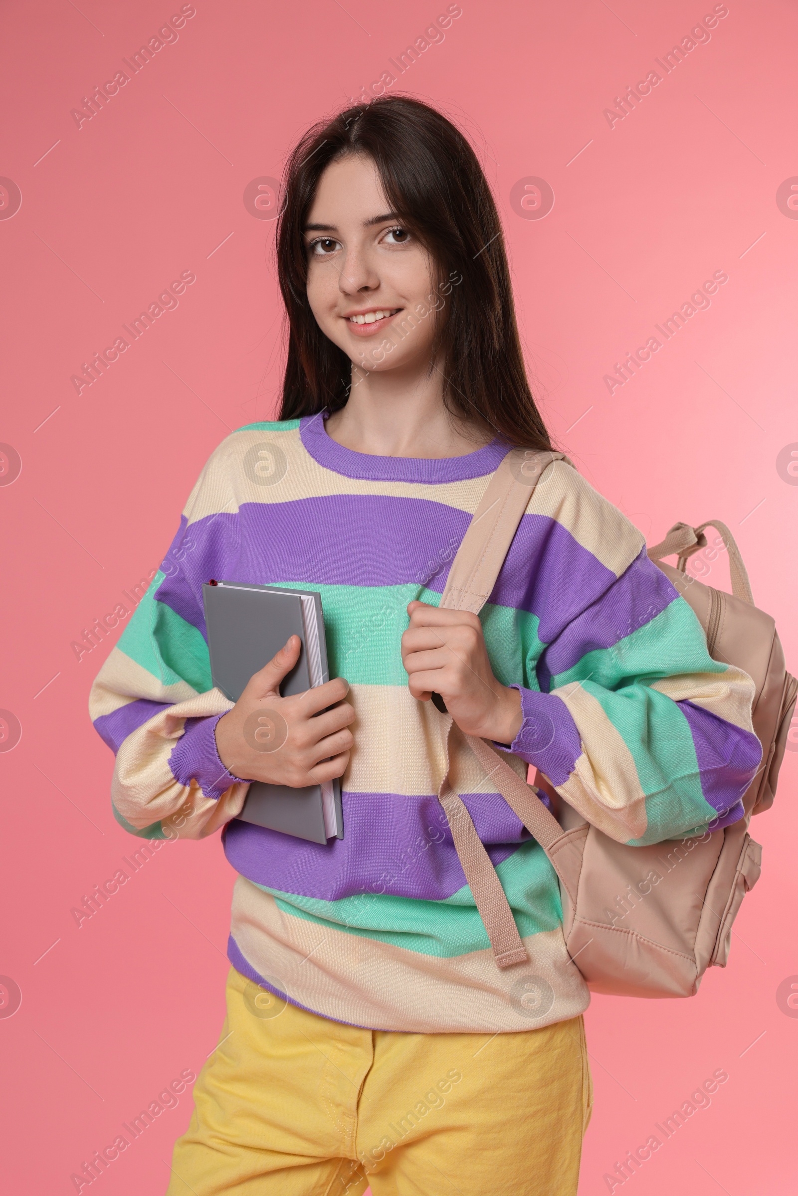 Photo of Cute teenage girl with backpack and book on pink background